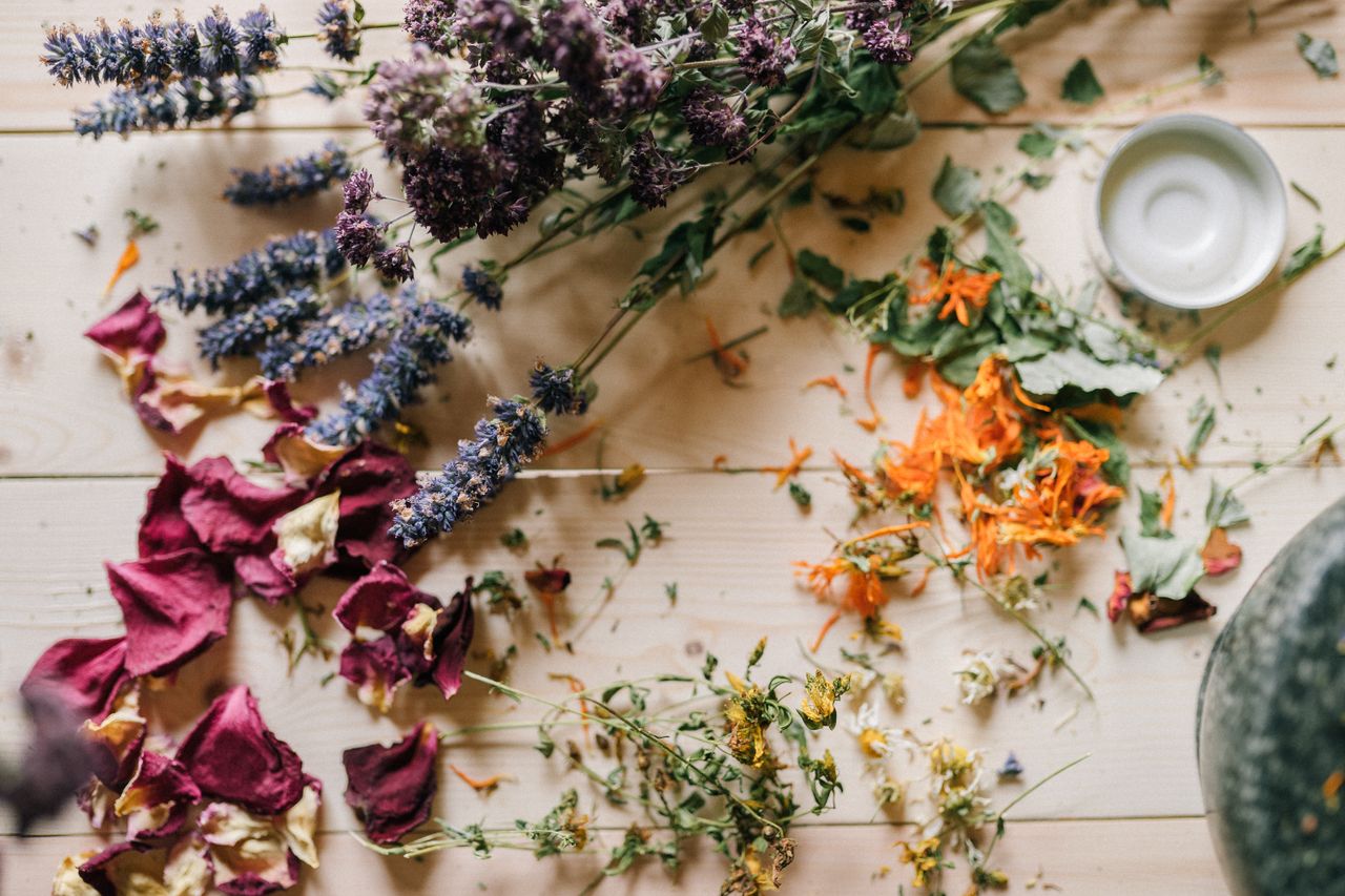 Home Assorted dried flowers and herbs scattered on a wooden table with a ceramic bowl.