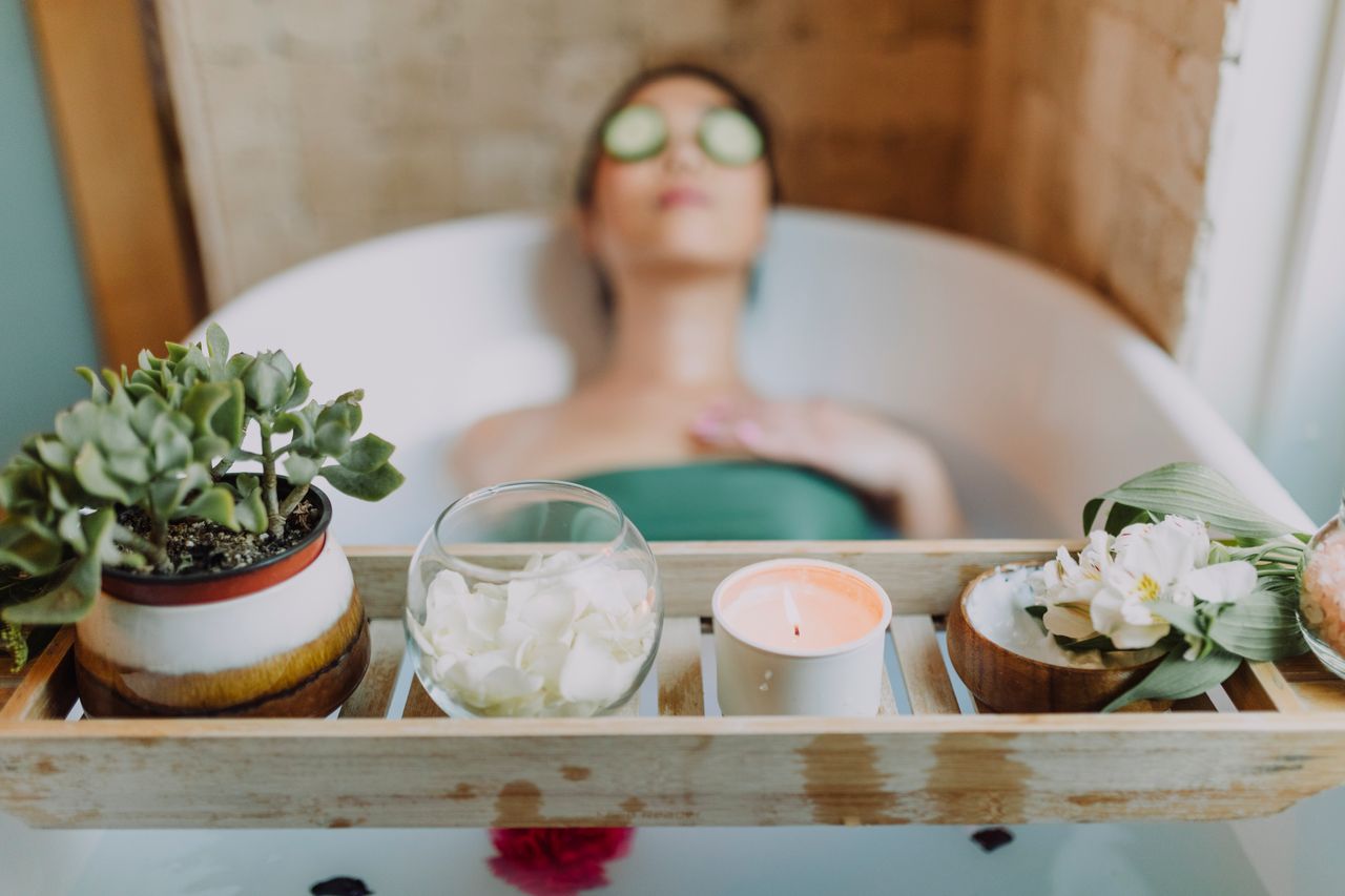 Home Woman relaxing in a bathtub with a candle and plants, enjoying a serene spa experience.